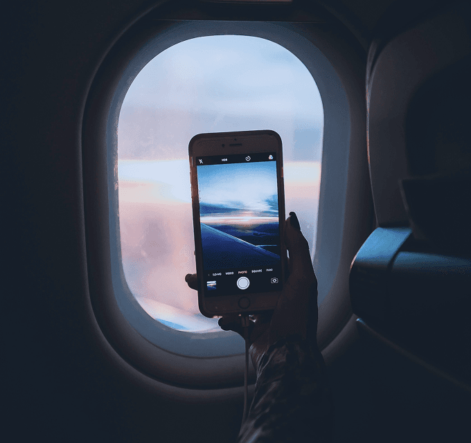 Hand holding a smartphone taking a photo through an airplane window